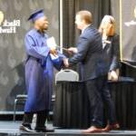 BHC president Dr. Jeremy Thomas handing certificate to GED grad Tony Johnson on stage
